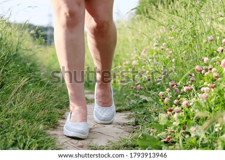 Woman running on a summer meadow overgrown with clover flowers. Slim female legs on a path, hiking and vacation on a nature