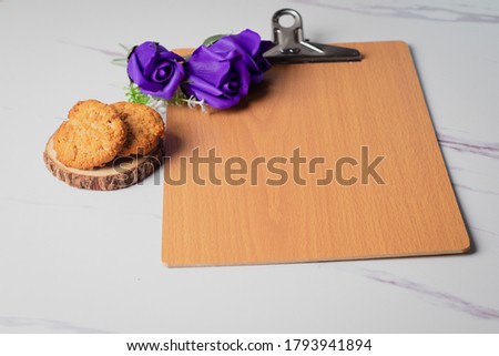 A wooden writing board on the side with purple roses and cookies on a white background.