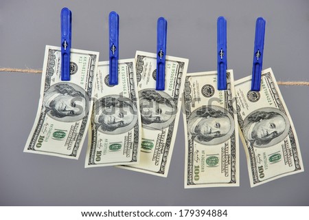 Dollar banknotes hanging on laundry line attached with plastic clothespins against gray background