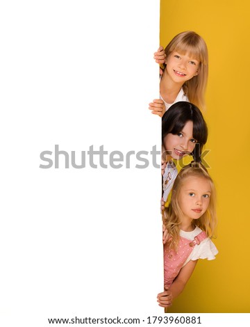 Group of three children of a girl with a white Board on a bright yellow background. Banner, free space for your ads, text. Billboard