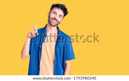 Young hispanic man wearing casual clothes showing and pointing up with finger number one while smiling confident and happy. 