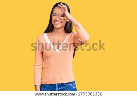 Young beautiful latin lady wearing casual clothes smiling happy doing ok sign with hand on eye looking through fingers 