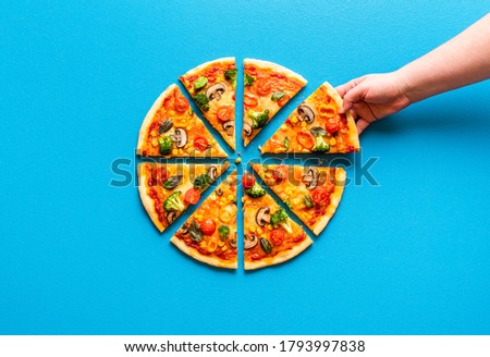 Above view with a woman's hand grabbing a slice of delicious homemade pizza. Vegetarian pizza with mozzarella, tomato sauce and plenty of fresh vegetables.