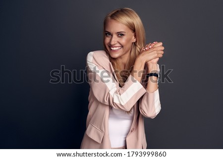 Close-up lovely, tender feminine young woman in pink trendy suit, clench hands together in tender and coquettish pose, smiling happily camera on grey background.