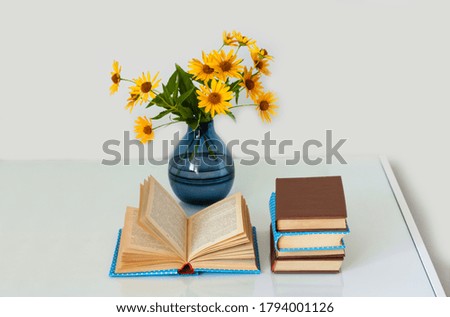 Cozy home interior decor: stack of books and vase with yellow flowers on a table. Distance home education.Quarantine concept of stay home