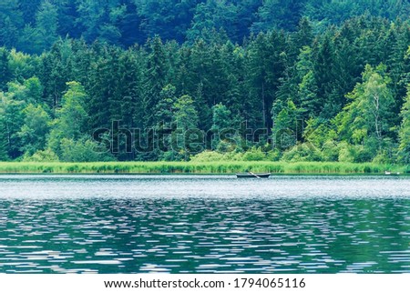 A boat with oars in the middle of a lake in a light rain. Large trees on the far side of the lake. Beautiful natural background. The concept of the beauty of nature in Europe. Dense forest by the lake