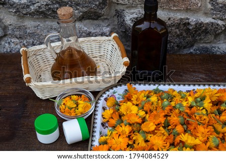 Calendula flowers are on the tray. Nearby are two jars of cream and a bottle of oil.