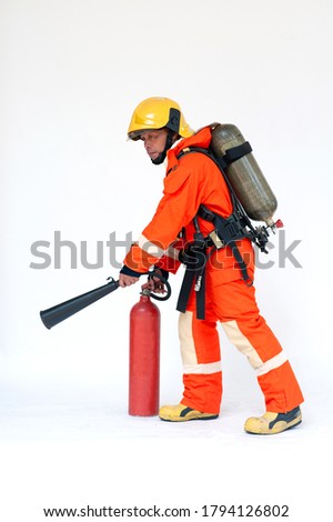 A portrait of Asian male firefighter in red protective uniform, mask and helmet with fire extinguisher standing on white background. 