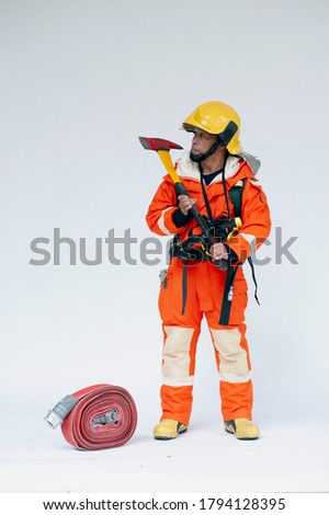 A portrait of Asian male fireman in red protective clothing, mask and helmet with an ax standing on a white background. 