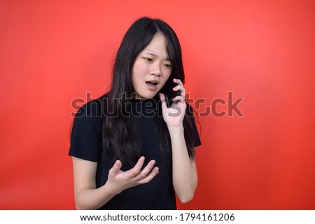 Portrait of Young beautiful asian woman using black T-shirt fight on phone with red isolated background