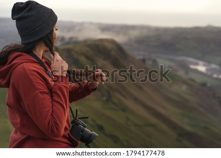 Woman with a camera touching her hair while standing at the top of a mountain. Travel concept