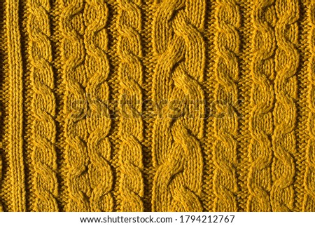 Background. A fragment of a knitted product in light mustard color. Volumetric knitting, vertical repeating pattern. autumn, winter fashion. Taken from above, lying flat