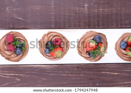 Cupcakes with whipped chocolate and berry, on wooden table. Picture for a menu or a confectionery catalog. Top view.