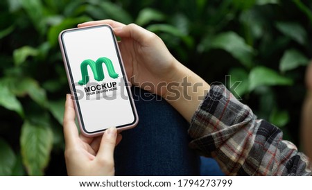 Close up view of a woman hands holding mock up smartphone while relaxed sitting in garden