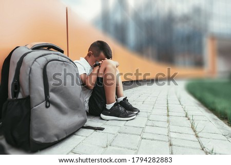 child with backpack in depression is sitting on the floor doesn't want back to school Royalty-Free Stock Photo #1794282883