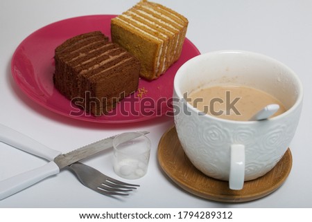 Two slices of honey cake. One of them is with chocolate. Dessert for Breakfast. Next to it is a mug of tea with milk and a beaker of pills.
