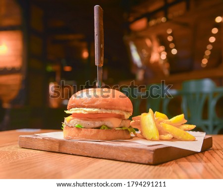Delicious juicy chef cheeseburger served with fries on a rustic wooden board on a table in bar or restaurant. Selective focus, blurred background. Junk food, fast food concept.