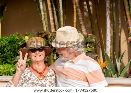 Happy retired couple in love enjoying summer vacation in a tropical garden under the bright sunlight with straw hats - active retired senior and fun concept