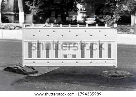 Plastic Protective barrier fence on the site of road work. Road sign standing on the road being repaired, monochrome shot
