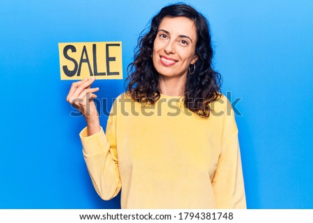 Young beautiful hispanic woman holding sale poster looking positive and happy standing and smiling with a confident smile showing teeth 