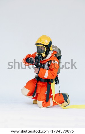 A portrait of Asian male firefighter in orange protective uniform, mask and helmet with fire extinguisher sitting on white background.  