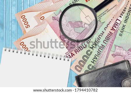 5000 Indonesian rupiah bills and magnifying glass with black purse and notepad. Concept of counterfeit money. Search for differences in details on money bills to detect fake