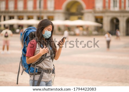 new normal Asian backpacker girl enjoying holidays travel in Europe - young happy and cute Chinese tourist woman in mask using mobile phone walking doing city tour