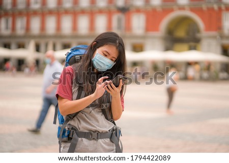 new normal Asian backpacker girl enjoying holidays travel in Europe - young happy and cute Chinese tourist woman in mask using mobile phone walking doing city tour