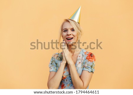 Image of excited cute woman in party cone expressing surprise on camera isolated over beige background. Celebration and fun.