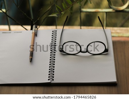 Eye glasses on desktop table surrounded by pen and notebook with natural view.