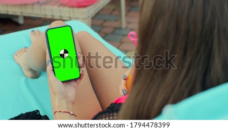 Woman Hands holding smartphone chrome key, tapping modern display smart phone. Close up of girl using mobile phone green screen while relaxing near the swimming pool in pink swimsuit.