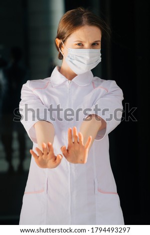 A portrait of a doctor's girlfriend in a medical mask and a woman holding her hands in front of her in a stop sign. The concept of protection