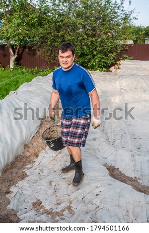 A man pours sand onto a geotextile outside. Garden work, do-it-yourself pool