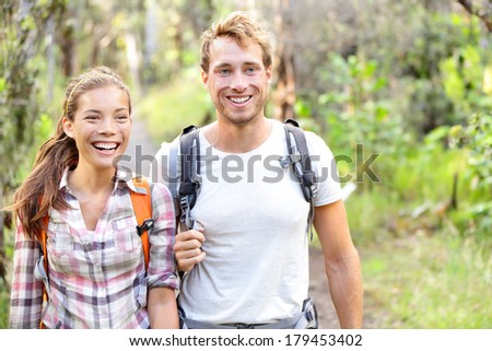 Hiking - hikers walking happy in forest. Hiker couple laughing and smiling. Interracial couple, Caucasian man and Asian woman on Big Island, Hawaii, USA.