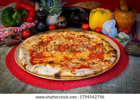 Pizza with tomato sauce, served with mozzarella cheese, spianata sausage, sweet peppers, on a table with food decoration.