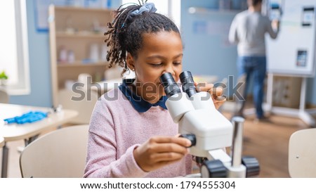 Portrait of Smart Little Schoolgirl Looking Under the Microscope. In Elementary School Classroom Cute Girl Uses Microscope. STEM (science, technology, engineering and mathematics) Education Program Royalty-Free Stock Photo #1794555304