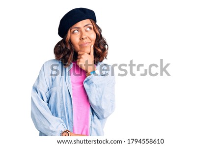 Young beautiful mixed race woman wearing french look with beret with hand on chin thinking about question, pensive expression. smiling with thoughtful face. doubt concept. 