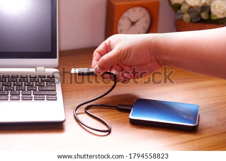 Man's hand was connecting an external portable hard disk usb 3.0 cable to laptop computer on desk, Data transfer or backup personal files concept