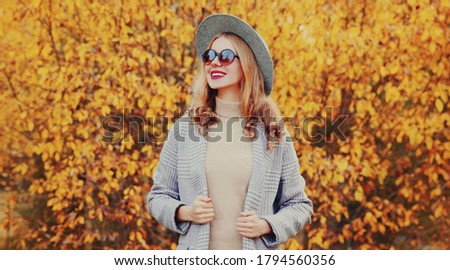 Autumn portrait stylish happy smiling woman wearing gray coat, round hat posing on yellow leaves background