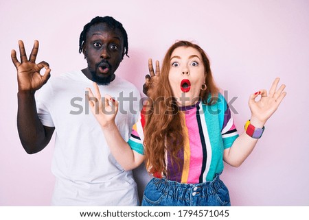Interracial couple wearing casual clothes looking surprised and shocked doing ok approval symbol with fingers. crazy expression 
