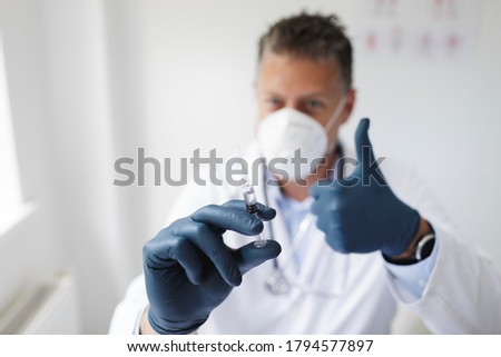 Doctor with nose and mouth mask holds syringe with the remedy against covid 19 