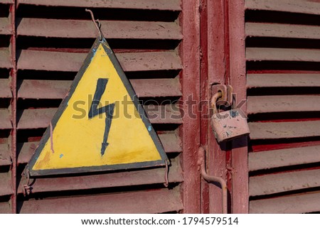 old red padlock covered with rust on a red door next to a yellow danger sign