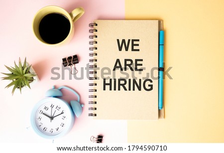 Creative top view flat lay with we are hiring text on notepad with copy space, bright minimal style. With alarm clock. Concept of new job hiring recruitment process, screening of new team members.