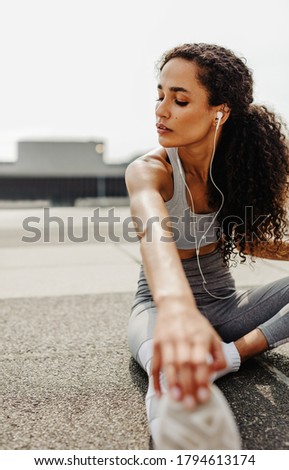 Fitness woman sitting outdoors and stretching. Sporty woman doing some stretching exercises in morning.
