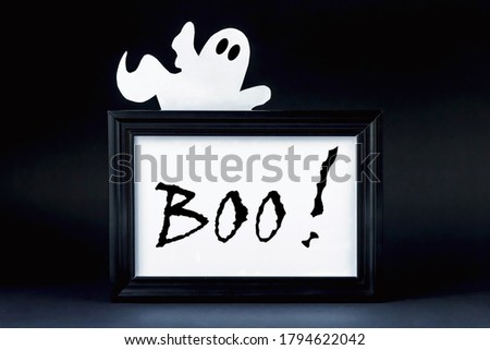 Background for Halloween. Black frame with BOO! on a black background. A white ghostly figure peeks out from behind the black lettering. Halloween typography concept. Halloween ideas.