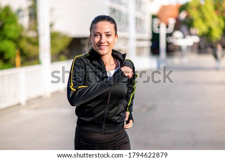 Closeup of a young smiling woman runner in black long sleeve track suit, running across the bridge on a sunny day Royalty-Free Stock Photo #1794622879