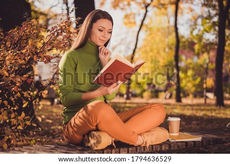 Photo of lovely charming intelligent lady come autumn park read romantic novel sit bench among trees crossed legs hand chin thinking wear green turtleneck orange pants sneakers outdoors