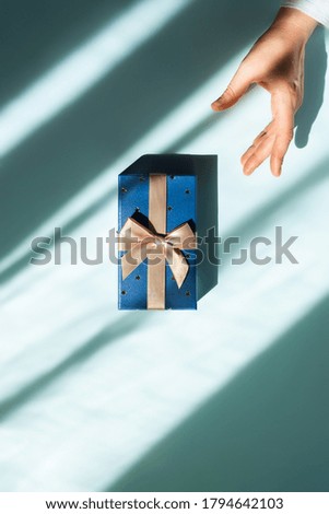 A gift in the center of the table and a woman's hand reaching for it. Flat lay picture.