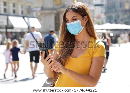Travel concept. Beautiful young traveler woman with protective mask using application map on smart phone. Tourist girl exploring city with mobile phone.
