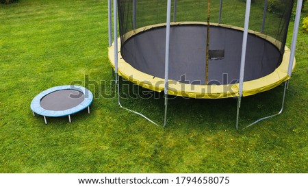 small trampoline near big one with round mat, size comparison, green lawn background